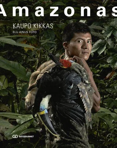Amazonas - Kaupo Kikkas (Go Group, 2013). Fotorealistlik kaanepilt kujutab noort põlisrahvaste meest tihedas rohelises vihmametsa taustal, kes hoiab kätel suurt eksootiliste sulgedega lindu. Tumedate toonidega foto on stiililt dokumentaalne ja atmosfäärikas.