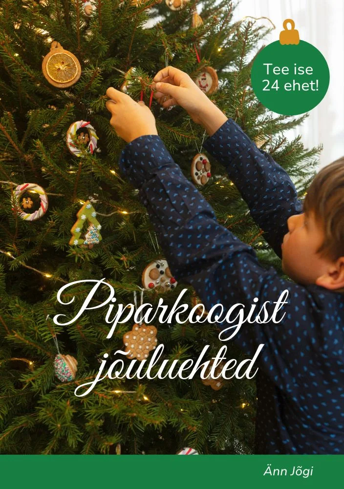 Piparkoogist jõuluehted - Änn Jõgi (2025). Fotorealistlik kaanepilt, millel laps ehtib rohelist jõulukuuske käsitööliste kaunistustega, taustal sädelevad tuled. Soe, hubane jõulutunnetus pehmetes rohelistes ja pruunides toonides.